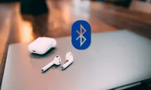 Auriculares inalámbricos y el logo de Bluetooth sobre un portátil. Guía para conectar auriculares bluetooth a pc.