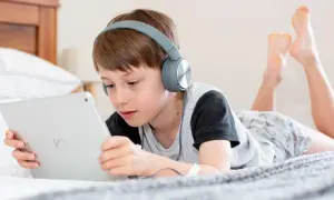 Niño con auriculares escucha atentamente mientras aprende a configurar iPad para niños en la cama.