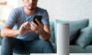 Hombre en sofá usa móvil mientras altavoz inteligente espera órdenes en modo super alexa.