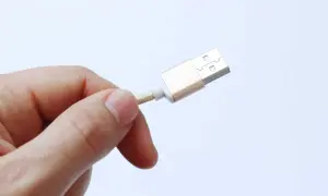 Dedo sujetando un cable USB dorado, advirtiendo sobre el peligro de juice jacking al conectar dispositivos en lugares públicos.