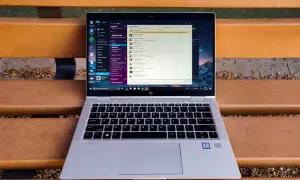Portátil HP EliteBook abierto en un banco de madera, mostrando la interfaz de Windows 10 con una aplicación de mensajería. Ideal para descubrir trucos Windows 10.