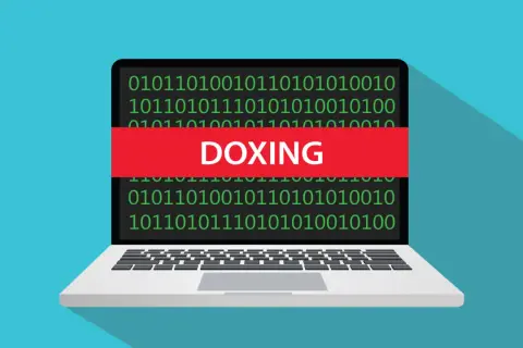 Portátil con código binario y una banda roja que dice "DOXING", ilustrando el doxeo que es.