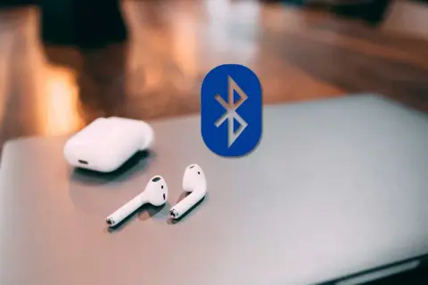 Auriculares inalámbricos y el logo de Bluetooth sobre un portátil. Guía para conectar auriculares bluetooth a pc.