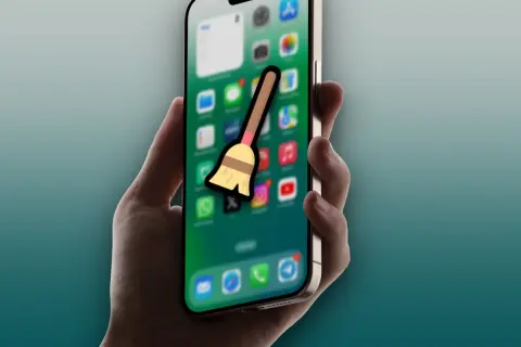 Mano sujetando un iPhone con iconos de apps y una escoba, sugiriendo la acción de borrar caché del iPad.