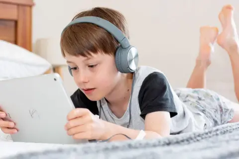 Niño con auriculares escucha atentamente mientras aprende a configurar iPad para niños en la cama.
