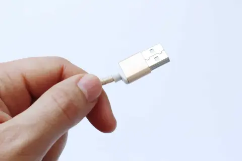 Dedo sujetando un cable USB dorado, advirtiendo sobre el peligro de juice jacking al conectar dispositivos en lugares públicos.