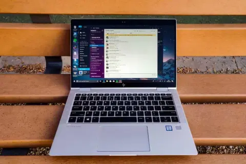 Portátil HP EliteBook abierto en un banco de madera, mostrando la interfaz de Windows 10 con una aplicación de mensajería. Ideal para descubrir trucos Windows 10.