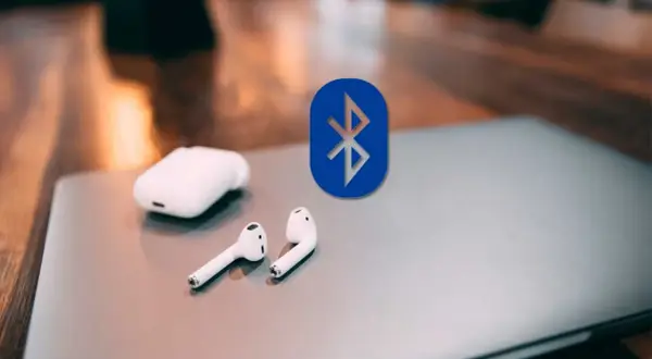 Auriculares inalámbricos y el logo de Bluetooth sobre un portátil. Guía para conectar auriculares bluetooth a pc.