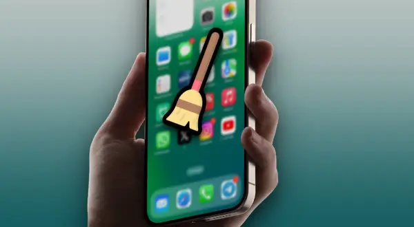 Mano sujetando un iPhone con iconos de apps y una escoba, sugiriendo la acción de borrar caché del iPad.