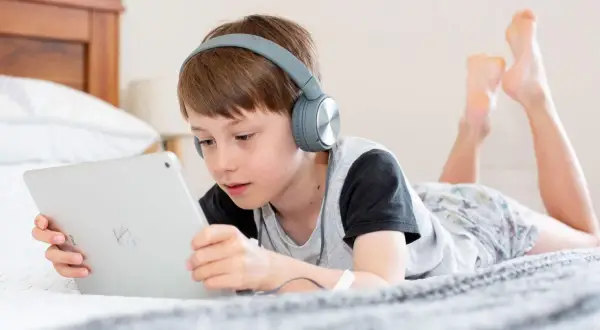 Niño con auriculares escucha atentamente mientras aprende a configurar iPad para niños en la cama.