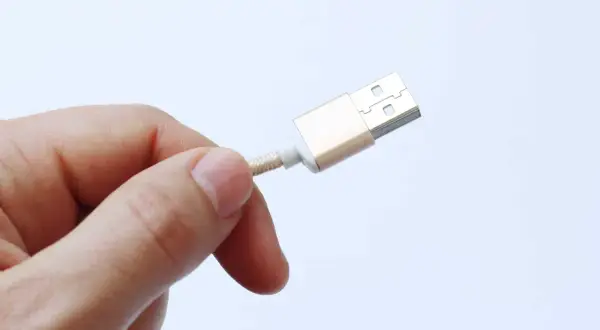 Dedo sujetando un cable USB dorado, advirtiendo sobre el peligro de juice jacking al conectar dispositivos en lugares públicos.