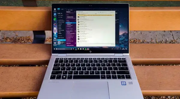 Portátil HP EliteBook abierto en un banco de madera, mostrando la interfaz de Windows 10 con una aplicación de mensajería. Ideal para descubrir trucos Windows 10.