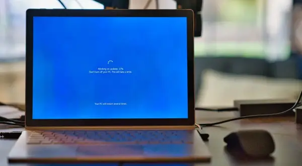 Un ordenador portátil muestra una pantalla azul de Windows con el mensaje "Working on updates 27%". El proceso de formatear ordenador está en marcha.