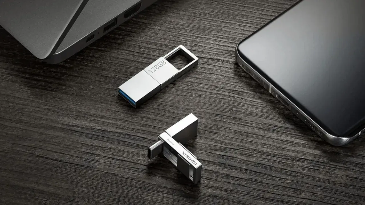 Dos unidades USB plateadas, una de 128GB y otra con logo Xiaomi, junto a un portátil y un smartphone. Perfectas para tus aplicaciones portables.