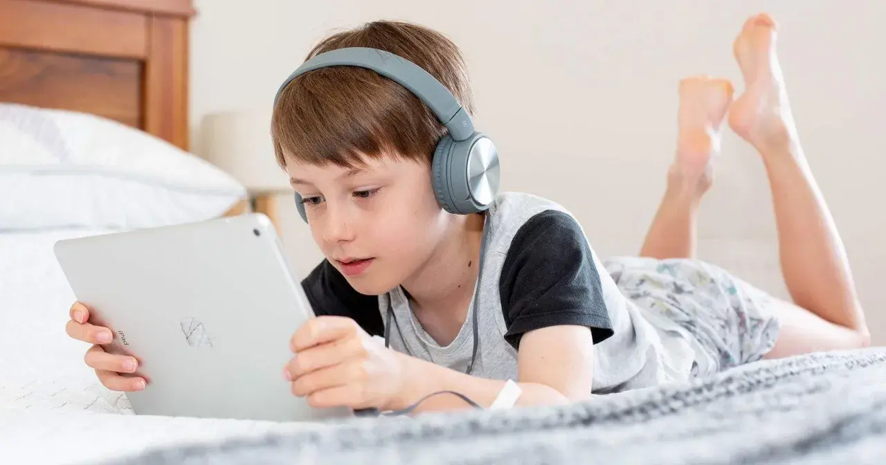 Niño con auriculares escucha atentamente mientras aprende a configurar iPad para niños en la cama.