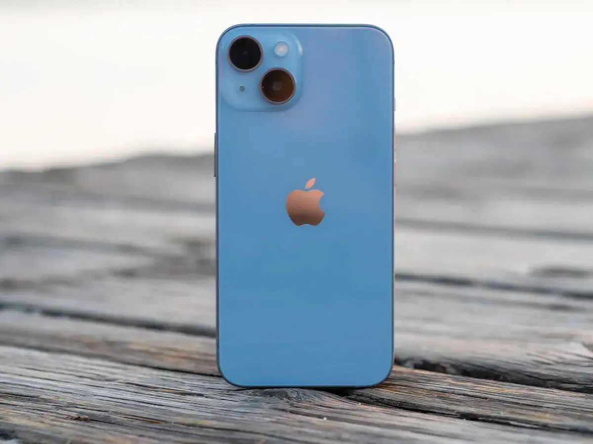 Un iPhone 14 azul descansa sobre madera. ¿Cuánto mide el iPhone 14? Sus dimensiones son perfectas para tu mano.