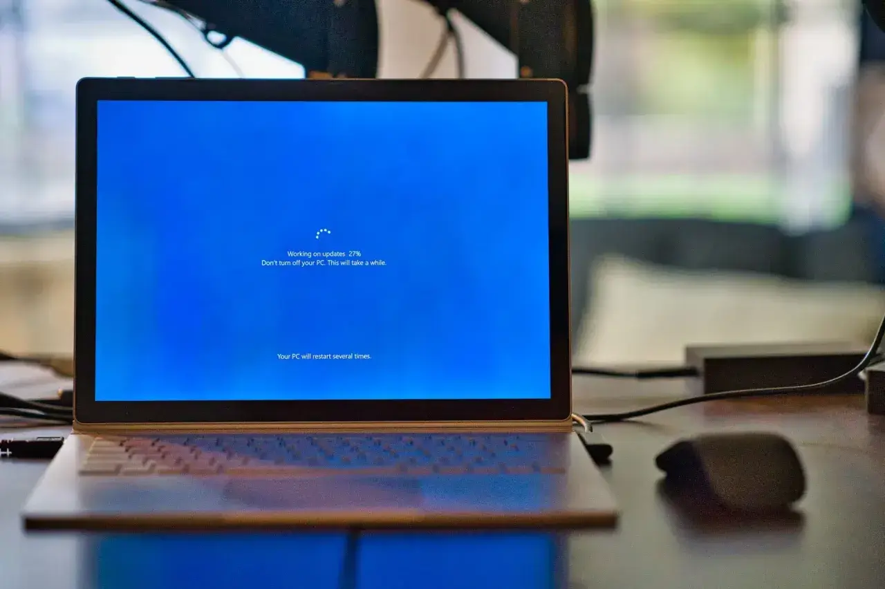 Un ordenador portátil muestra una pantalla azul de Windows con el mensaje "Working on updates 27%". El proceso de formatear ordenador está en marcha.