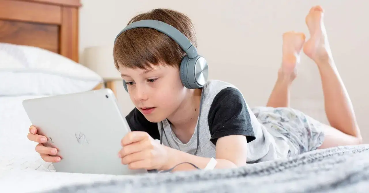 Niño con auriculares escucha atentamente mientras aprende a configurar iPad para niños en la cama.