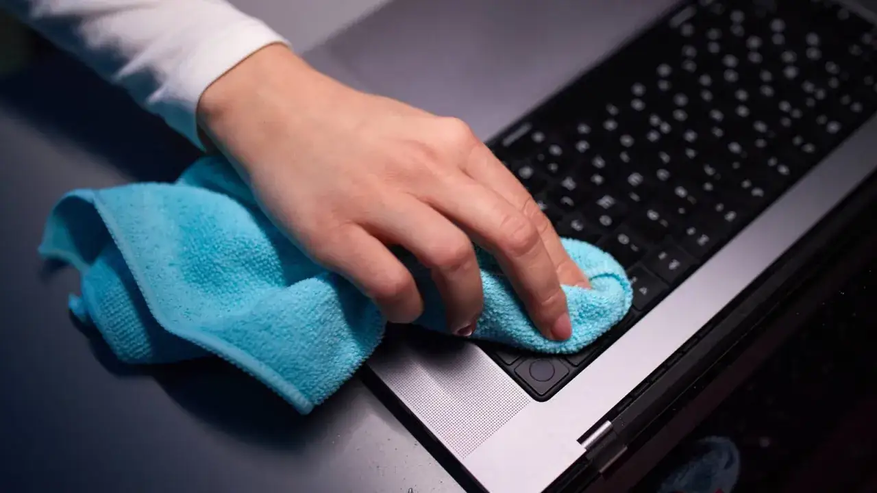 Mano limpiando el teclado de un Mac con un pa&ntilde;o azul. Un gesto para limpiar cache mac y mantener tu equipo impecable.