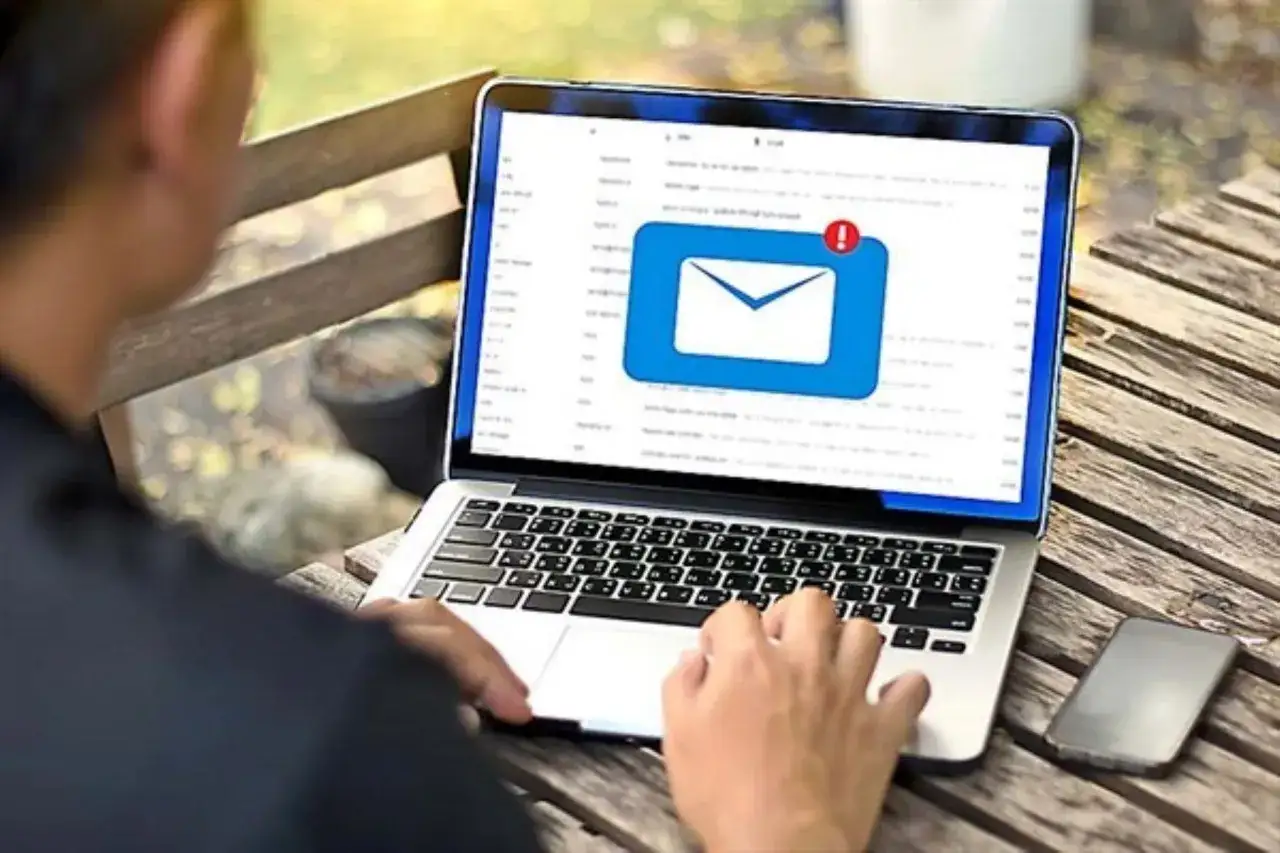 Persona usa laptop para aprender como dejar de recibir correos phishing. Icono de sobre con alerta.