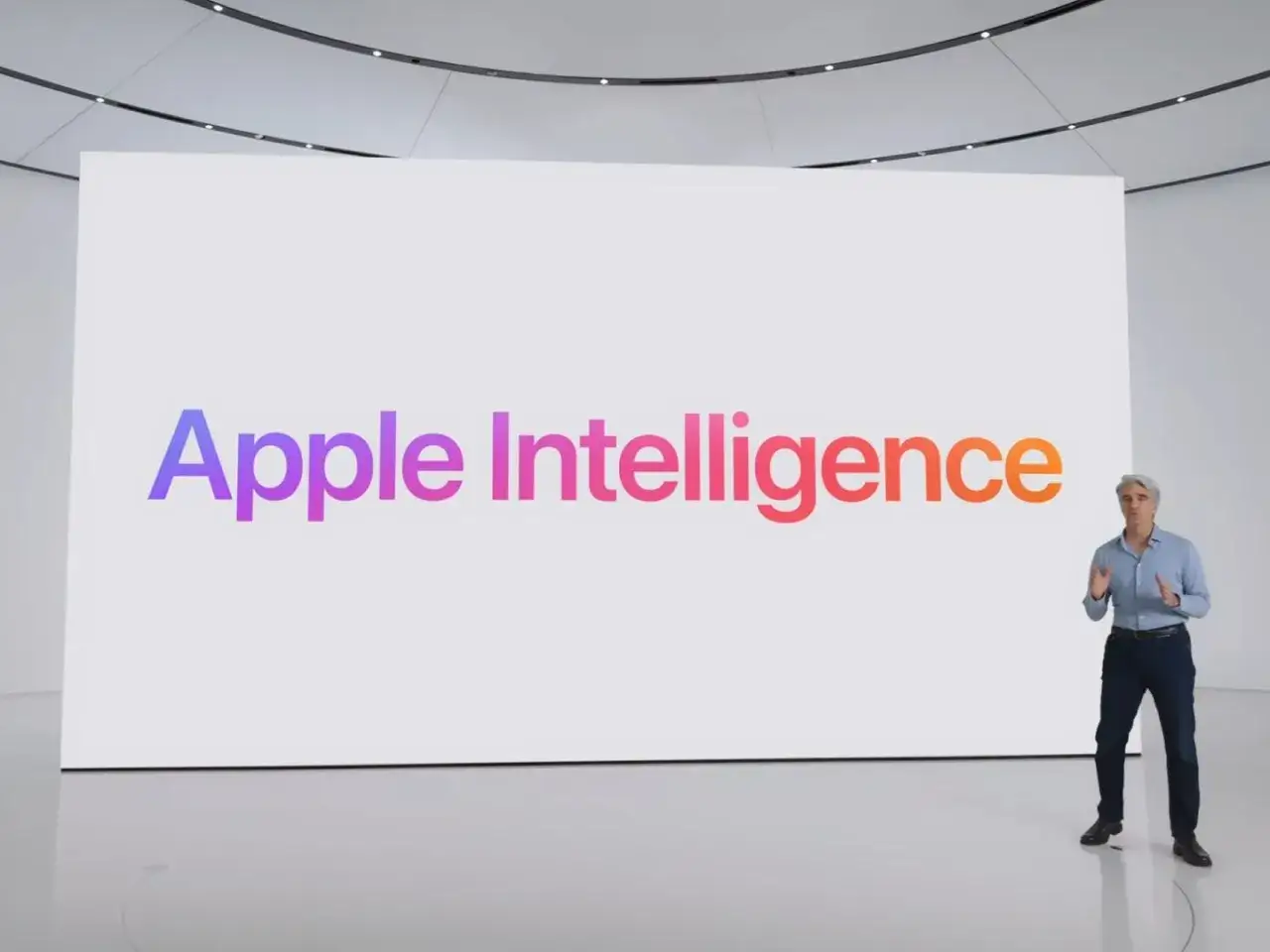 Presentación de Apple Intelligence en WWDC. Un hombre habla frente a una pantalla gigante con el logo de Apple Intelligence en degradado.