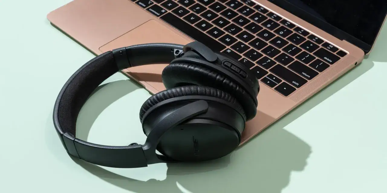 Auriculares negros Bose sobre un portátil rosa. Ideal para conectar auriculares bluetooth a pc y disfrutar de tu música.