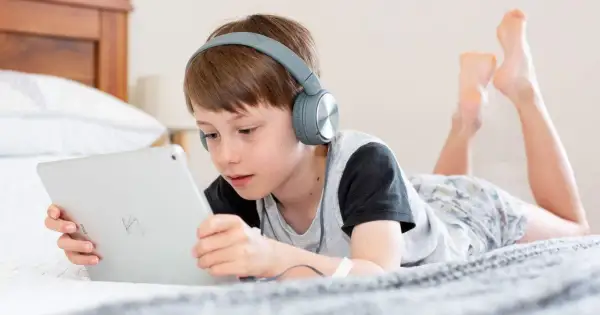 Niño con auriculares escucha atentamente mientras aprende a configurar iPad para niños en la cama.