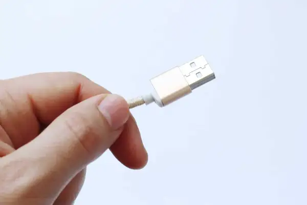 Dedo sujetando un cable USB dorado, advirtiendo sobre el peligro de juice jacking al conectar dispositivos en lugares públicos.