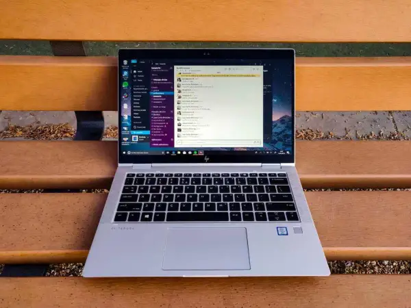 Portátil HP EliteBook abierto en un banco de madera, mostrando la interfaz de Windows 10 con una aplicación de mensajería. Ideal para descubrir trucos Windows 10.
